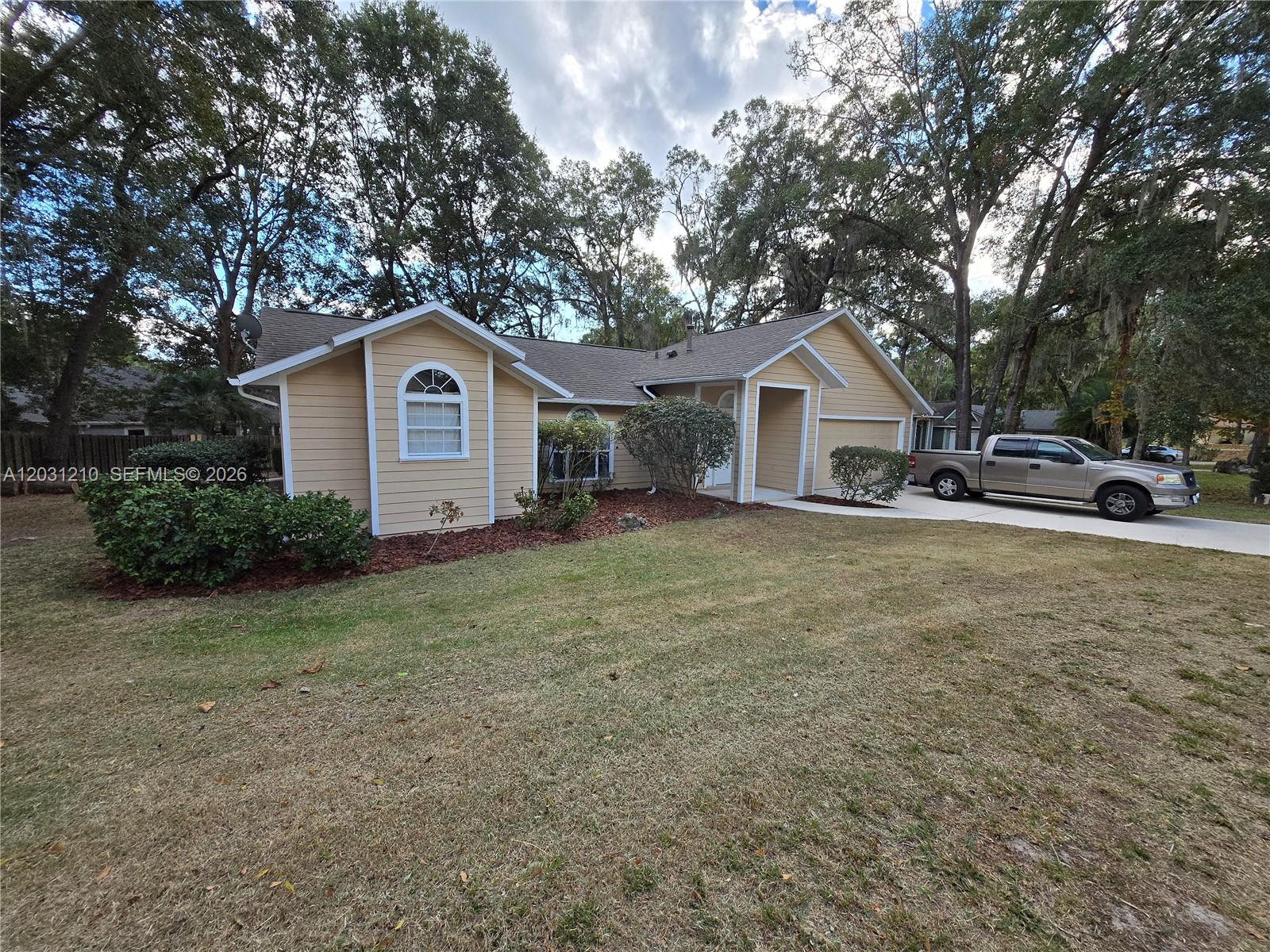 A tan, single-story house with a gabled roof and a driveway sits on a lawn — 8309 SW 61st Place # 1, Gainesville FL 32608, GAINESVILLE, FL