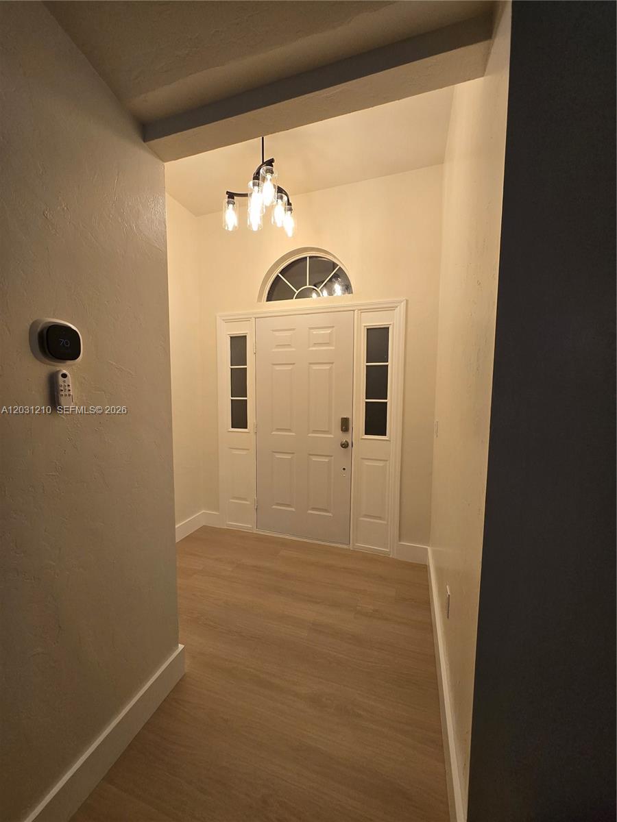 An entryway features light wood-look flooring, a white front door with sidelights, and a chandelier — 8309 SW 61st Place # 1, Gainesville FL 32608, GAINESVILLE, FL