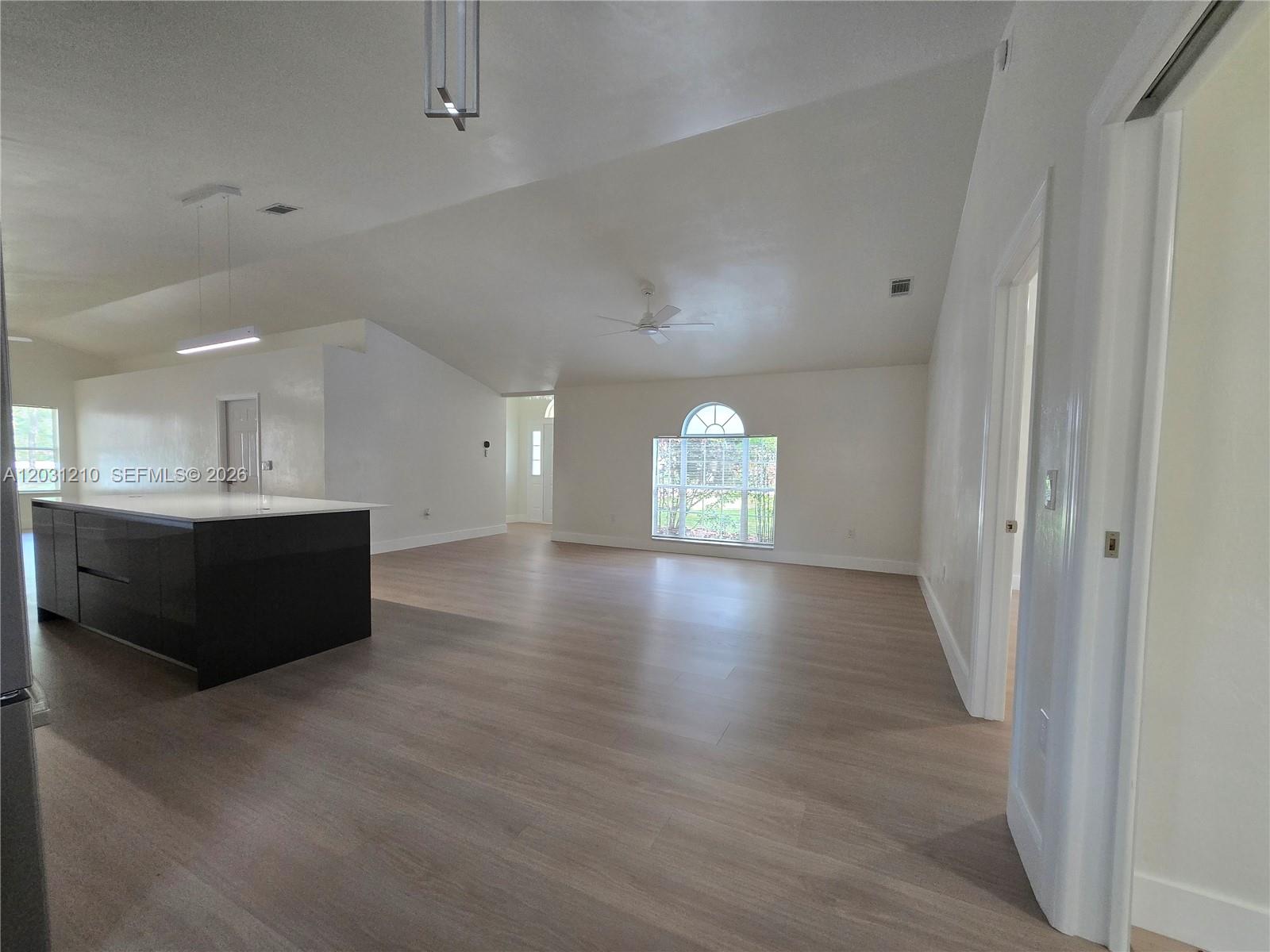 An open-concept living area features light wood flooring, a dark kitchen island, and vaulted ceilings — 8309 SW 61st Place # 1, Gainesville FL 32608, GAINESVILLE, FL