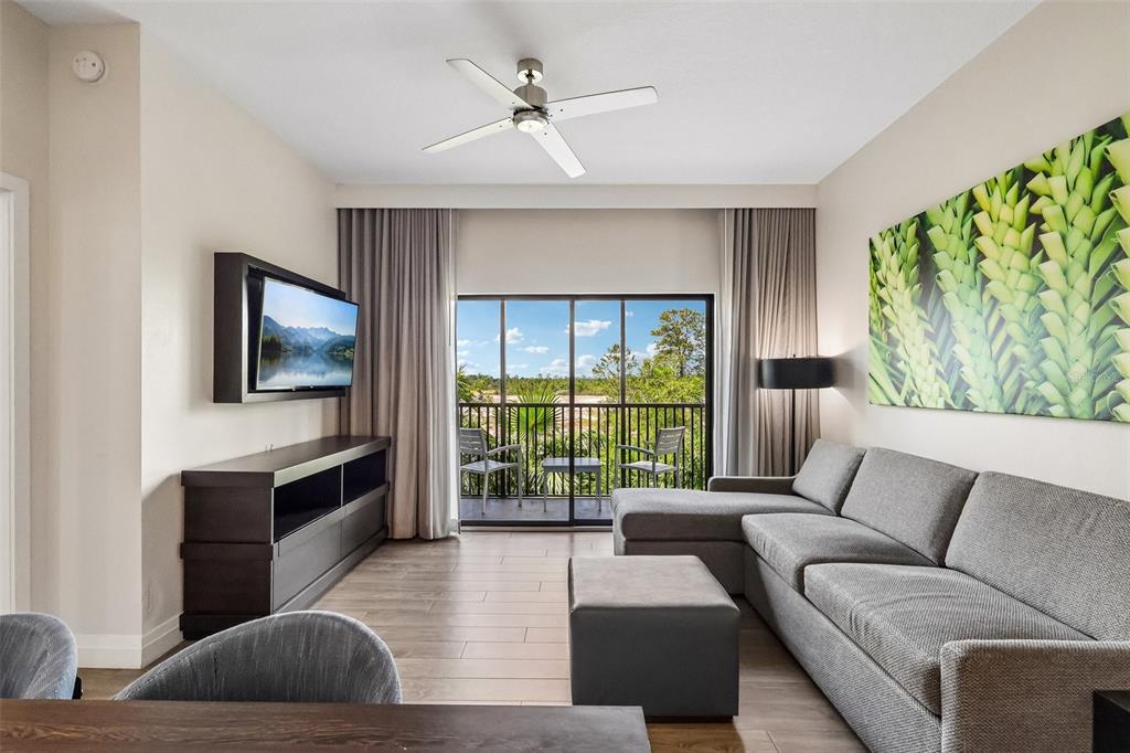 A living room features a gray sectional sofa, a television, and a balcony with outdoor seating — 14501 GROVE RESORT AVENUE UNIT 2342, WINTER GARDEN, FL
