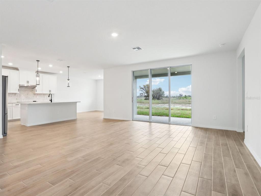 An open-concept living area features light wood-look tile flooring, a kitchen island, and sliding glass doors — 1705 DRAUGHTON DRIVE, ZEPHYRHILLS, FL