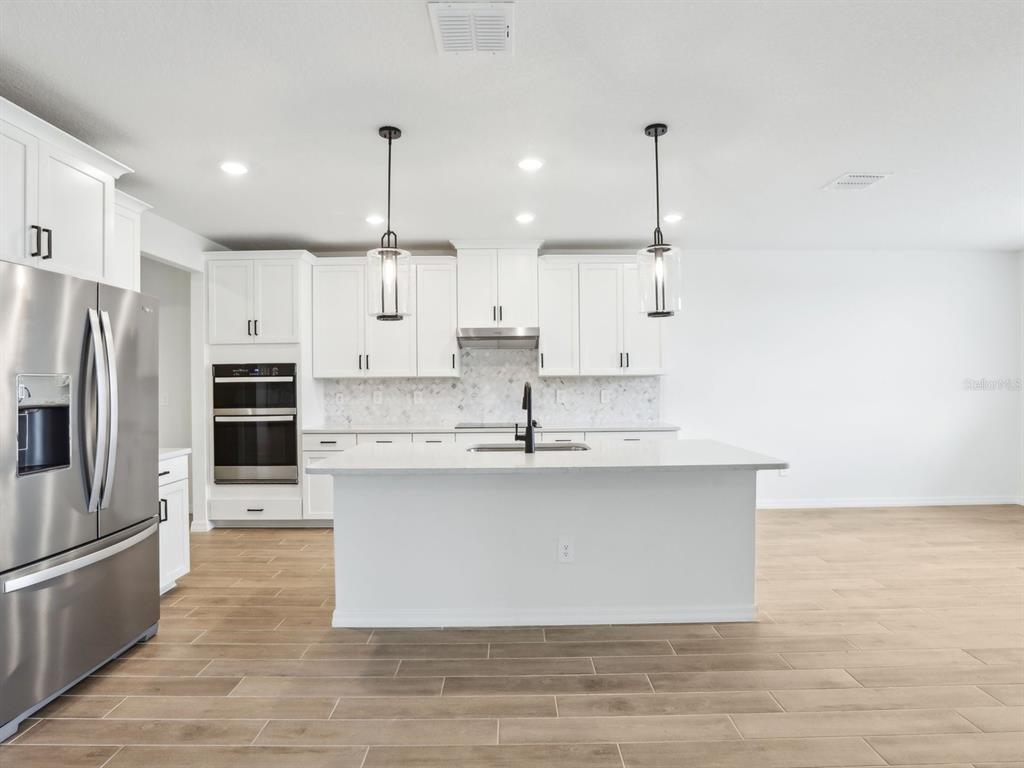 A modern kitchen features white cabinetry, stainless steel appliances, a center island, and wood-look flooring — 1705 DRAUGHTON DRIVE, ZEPHYRHILLS, FL