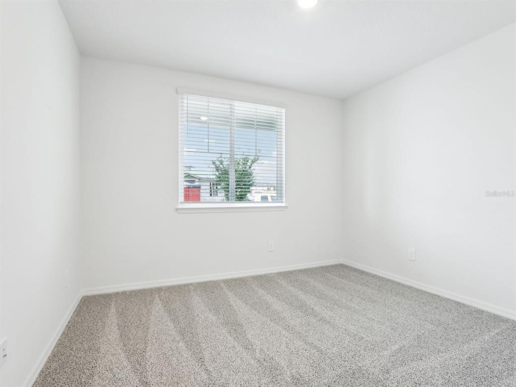 An empty bedroom features white walls, gray carpet, and a window with horizontal blinds — 1705 DRAUGHTON DRIVE, ZEPHYRHILLS, FL