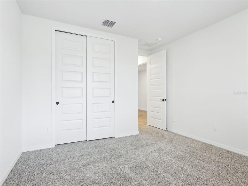 A bedroom features white walls, gray carpet, a sliding closet, and an open doorway — 1705 DRAUGHTON DRIVE, ZEPHYRHILLS, FL