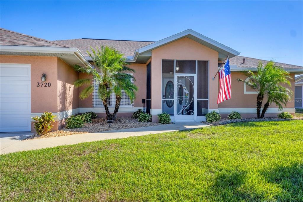A single-story house with a tan stucco exterior, a screened entryway, and a front lawn — 2720 S BISCAYNE DRIVE, NORTH PORT, FL