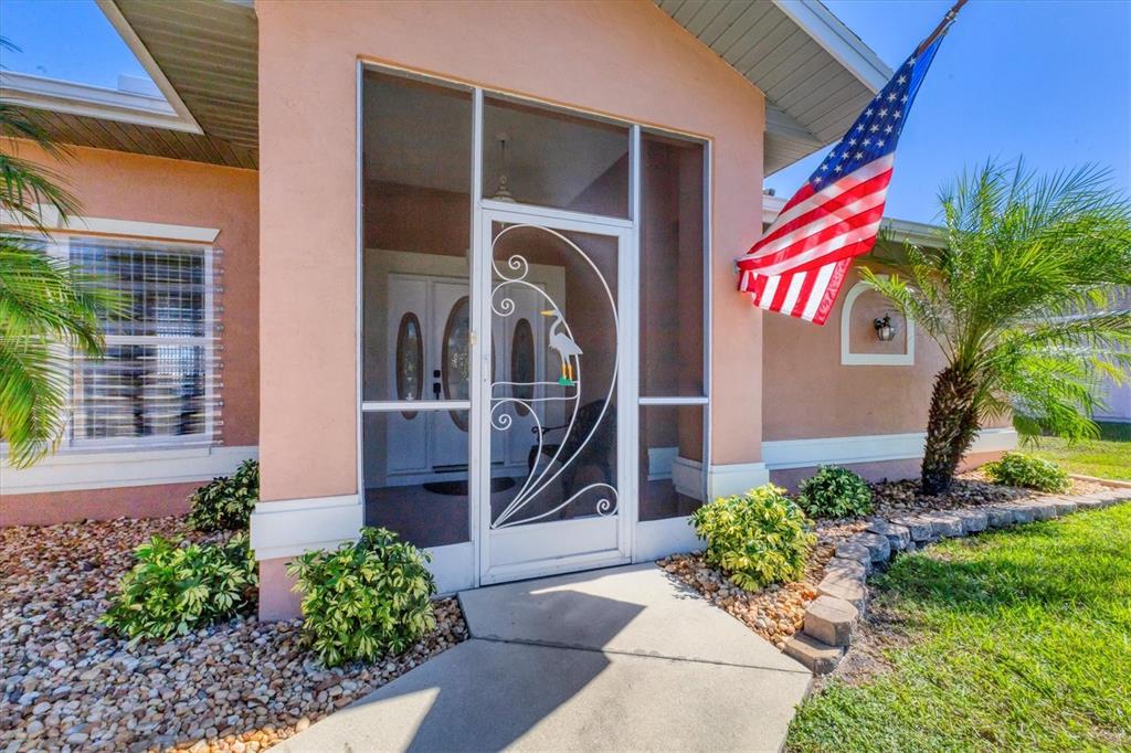 The exterior of a peach-colored house features a screened front entryway and an American flag — 2720 S BISCAYNE DRIVE, NORTH PORT, FL