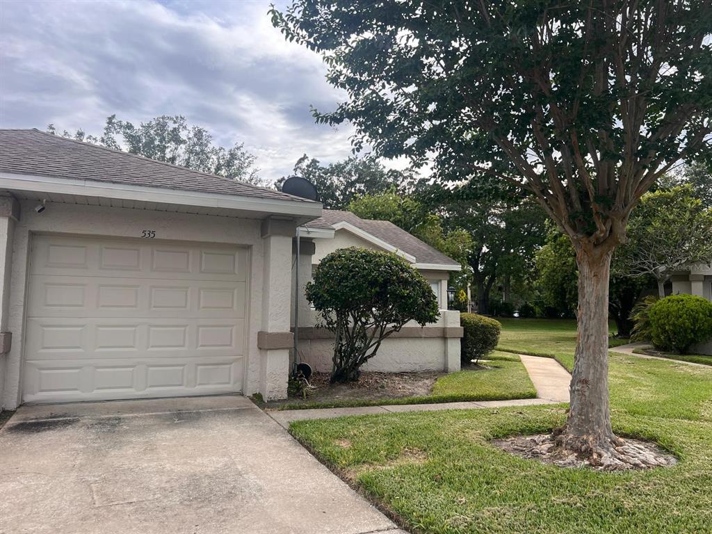 A single-story house exterior features a beige garage, a concrete driveway, and a large tree — 535 AZINGER CIRCLE UNIT 16, ORLANDO, FL