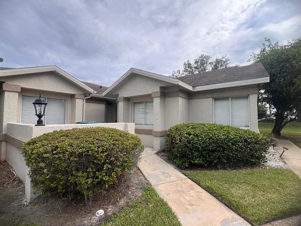 A single-story house exterior features beige stucco walls, a concrete walkway, and two large shrubs — 535 AZINGER CIRCLE UNIT 16, ORLANDO, FL