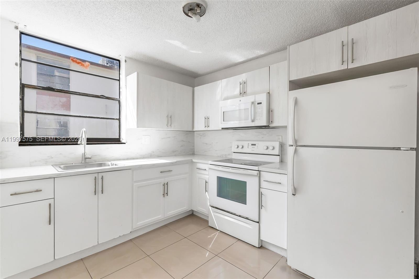 A bright kitchen features white cabinets, white appliances, a tiled floor, and a large window — 1798 NW 55th Ave # 202, Lauderhill FL 33313, LAUDERHILL, FL