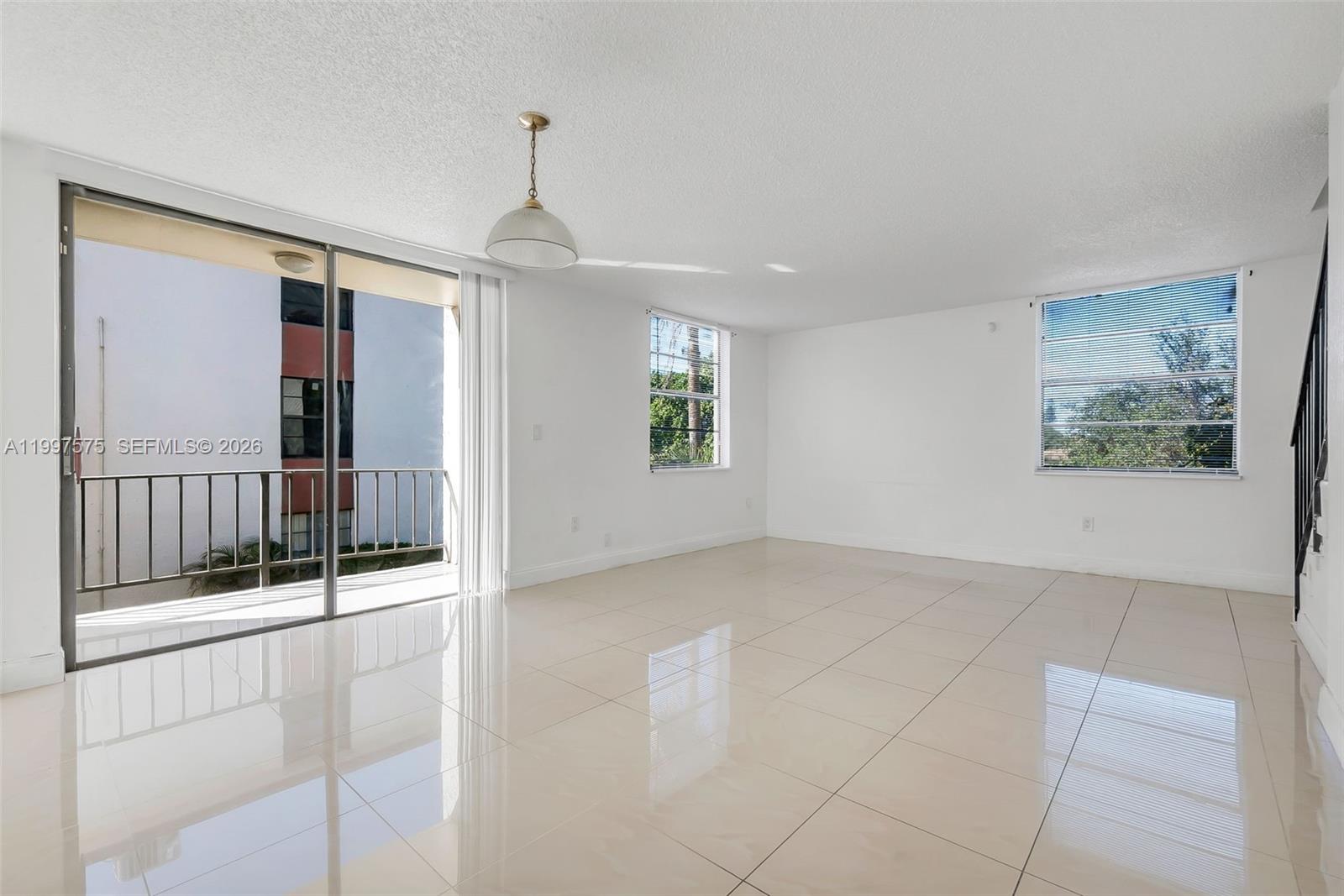 An empty living room features white walls, light-colored tile flooring, a balcony, and two windows — 1798 NW 55th Ave # 202, Lauderhill FL 33313, LAUDERHILL, FL