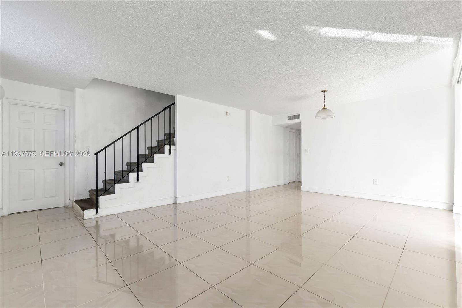 An empty room features white walls, tiled floors, and a staircase with a black railing — 1798 NW 55th Ave # 202, Lauderhill FL 33313, LAUDERHILL, FL
