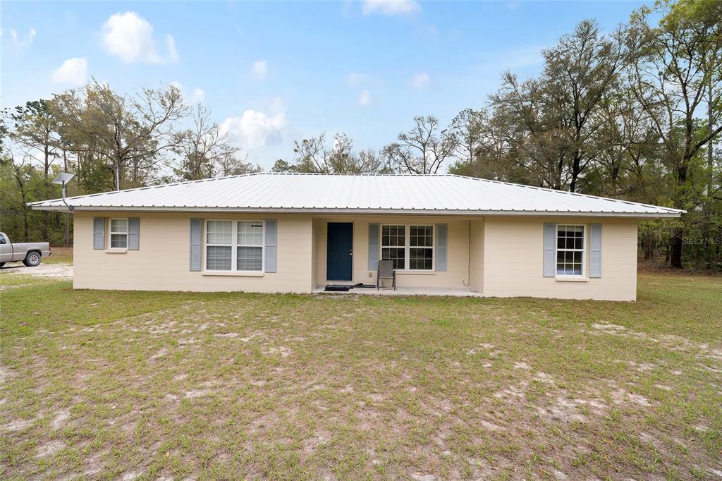 A single-story house with a light-colored exterior, a white metal roof, and a front porch — 2610 NE 80TH AVENUE, HIGH SPRINGS, FL