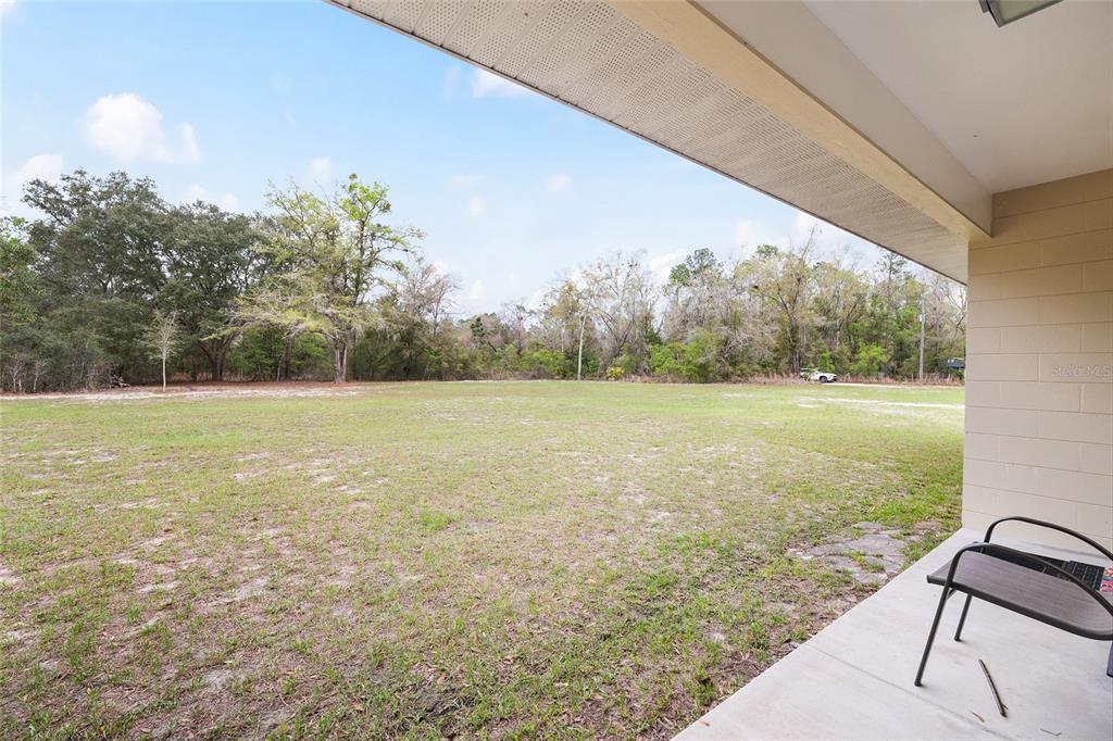 A concrete patio overlooks a large, grassy backyard bordered by a line of trees — 2610 NE 80TH AVENUE, HIGH SPRINGS, FL