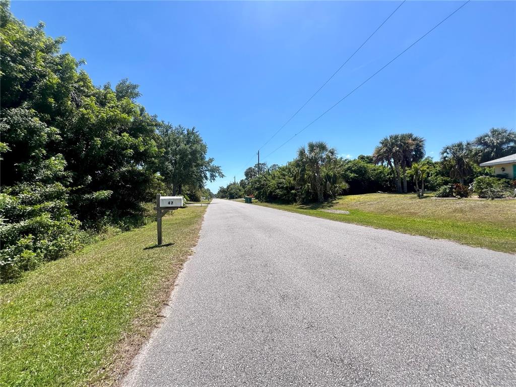 A paved road stretches into the distance, flanked by lush green trees and a mailbox — 48 RAMBLEWOOD STREET, PORT CHARLOTTE, FL
