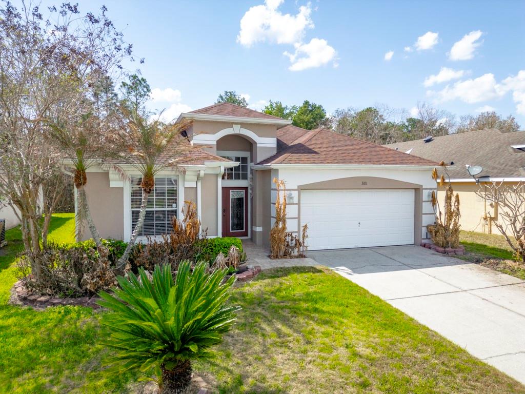 A single-story suburban house features a two-car garage, a front lawn, and palm trees — 3181 STONEHURST CIRCLE, KISSIMMEE, FL