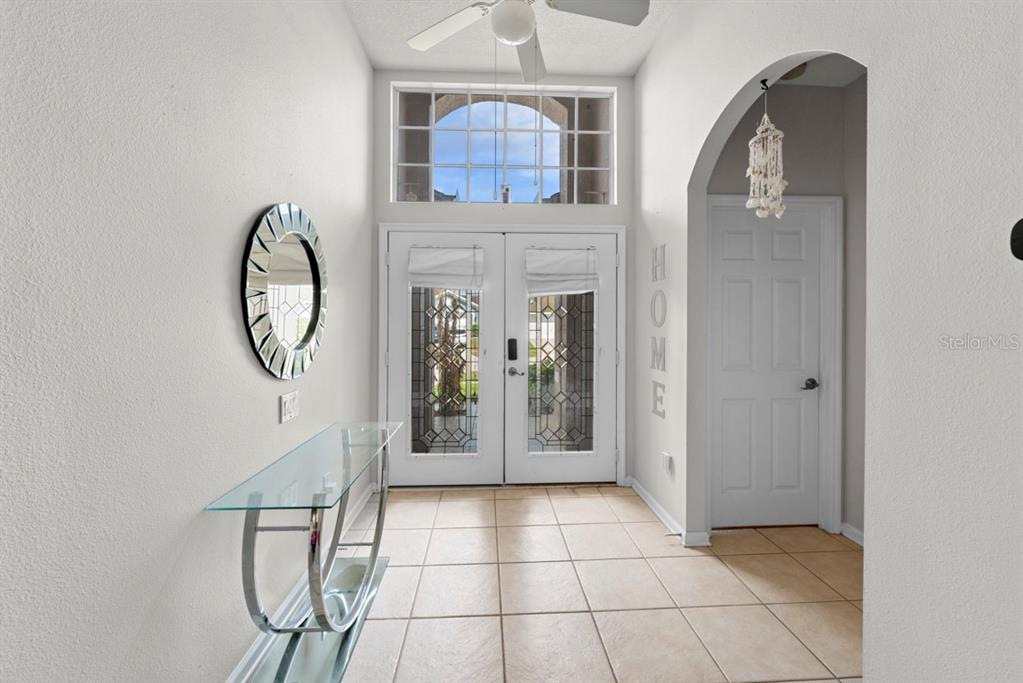 An entryway features a glass console table, a round mirror, and double doors with windows — 3181 STONEHURST CIRCLE, KISSIMMEE, FL