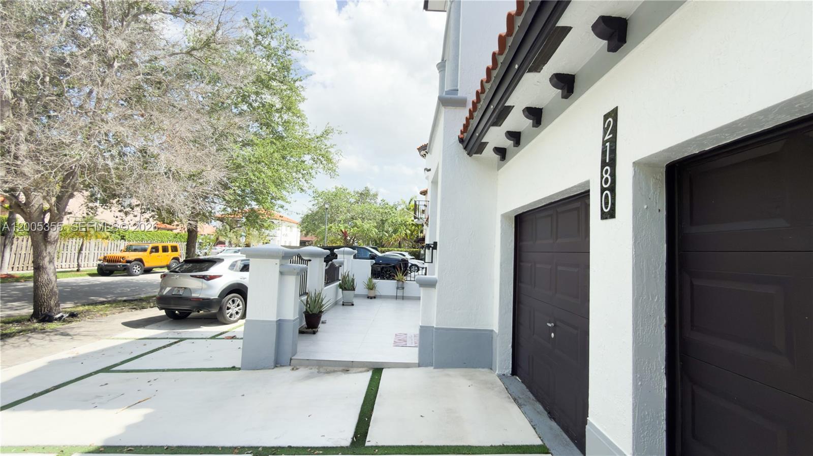 A white house exterior features a dark garage door, a tiled patio, and potted plants — 2180 SW 152nd Pl, Miami FL 33185, MIAMI, FL