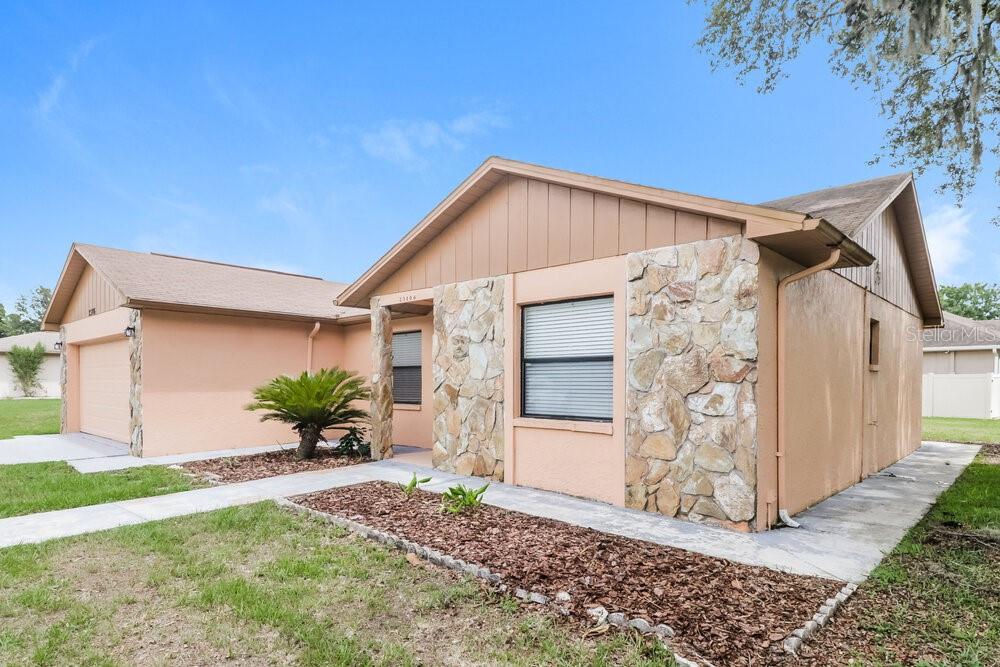 A single-story house with peach-colored stucco walls, a stone facade, and an attached garage — 23106 MAYFAIR ROAD, LAND O LAKES, FL