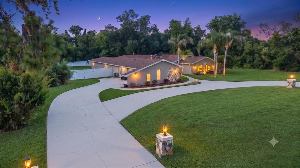 A single-story house with a stone accent wall and a curved concrete driveway at dusk — 7487 RIVER COUNTRY DRIVE, WEEKI WACHEE, FL