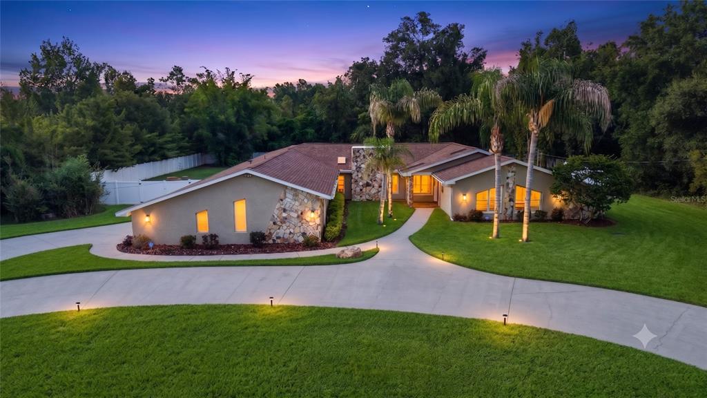 A single-story house with a stone facade and palm trees at dusk — 7487 RIVER COUNTRY DRIVE, WEEKI WACHEE, FL