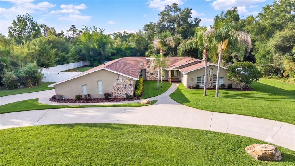 An aerial view of a single-story house with a stone facade and a curved driveway — 7487 RIVER COUNTRY DRIVE, WEEKI WACHEE, FL