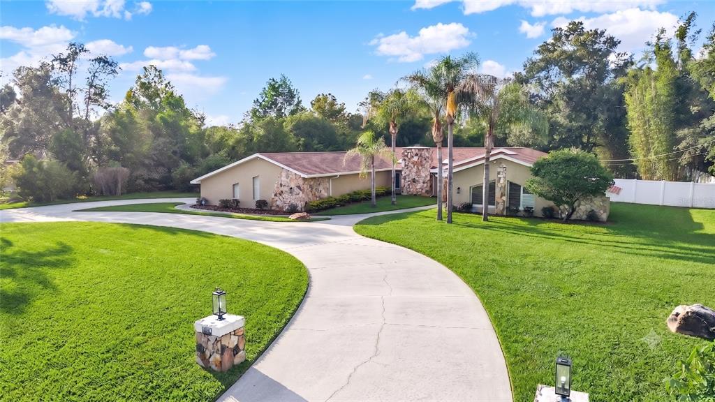 A single-story house with stone accents and a curved driveway sits on a grassy lot — 7487 RIVER COUNTRY DRIVE, WEEKI WACHEE, FL