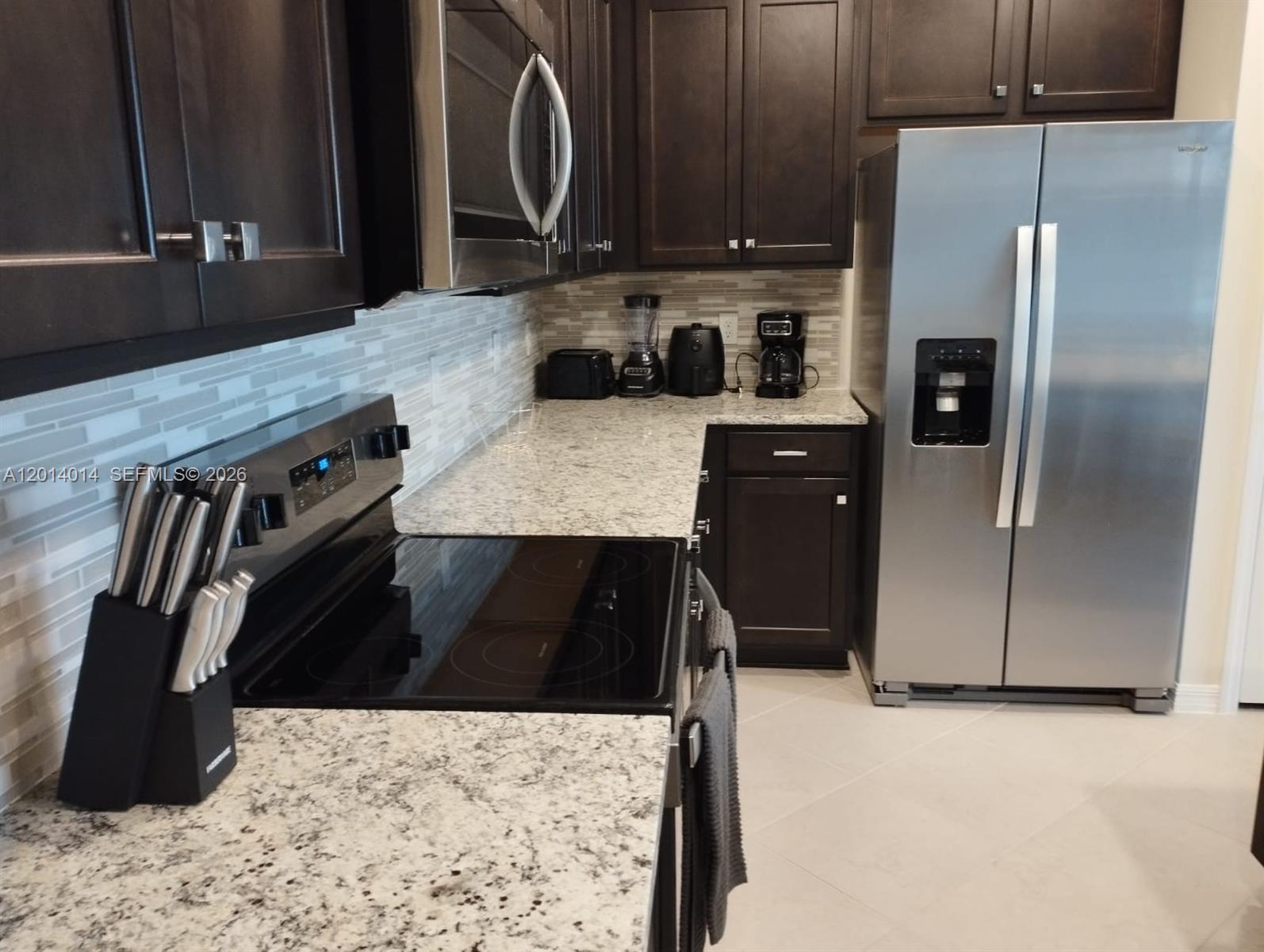 A kitchen features dark wood cabinets, granite countertops, stainless steel appliances, and a tiled backsplash — 1292 BLUE ISLAND DRIVE # 1292, Clermont FL 34714, CLERMONT, FL