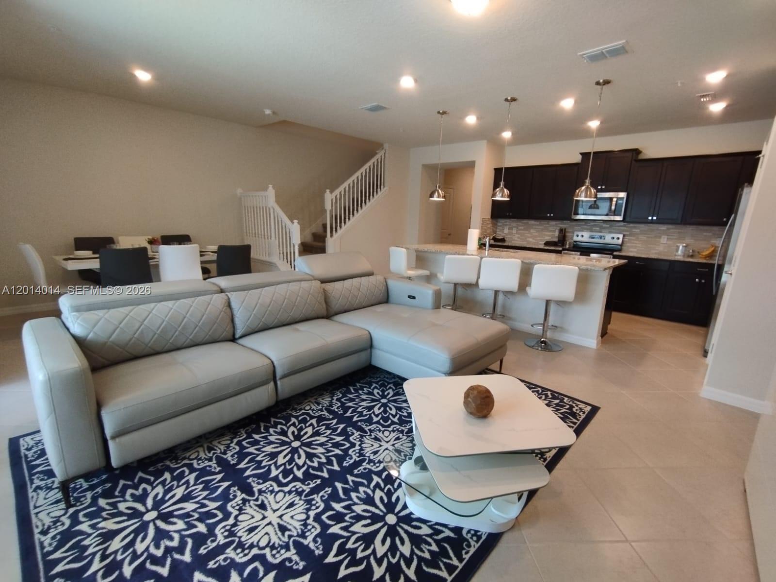 An open-concept living room features a gray sectional sofa, a patterned rug, and a kitchen — 1292 BLUE ISLAND DRIVE # 1292, Clermont FL 34714, CLERMONT, FL