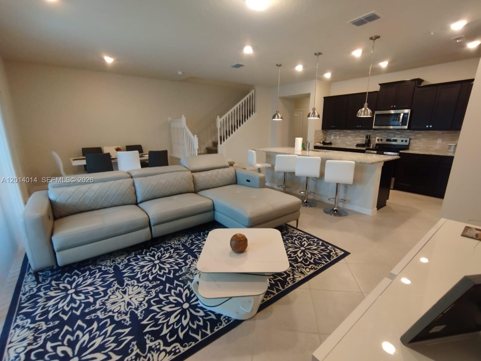 An open-concept living room features a grey sectional, patterned rug, and a kitchen with island — 1292 BLUE ISLAND DRIVE # 1292, Clermont FL 34714, CLERMONT, FL