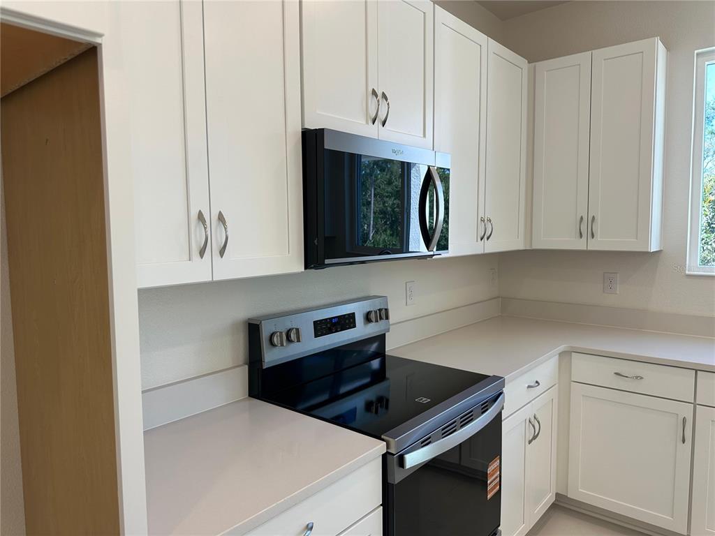 A kitchen features white cabinets, stainless steel appliances, and light-colored countertops — 3449 SANCTUARY DRIVE, CLERMONT, FL