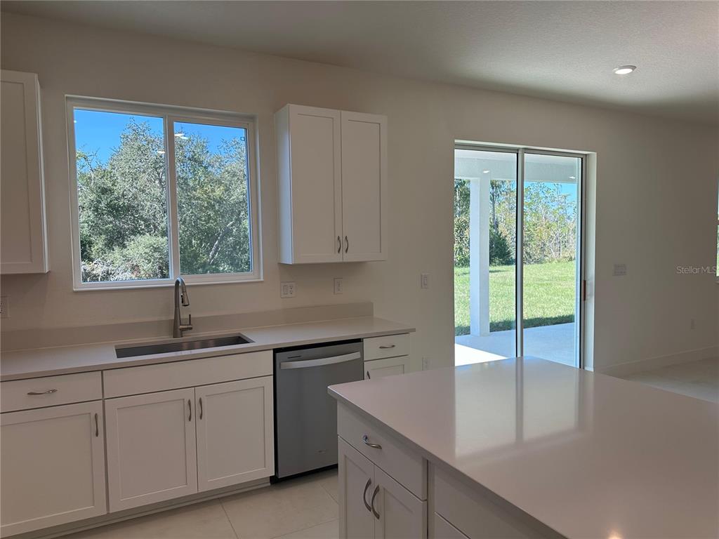 A kitchen features white cabinets, quartz countertops, a stainless steel dishwasher, and a sliding glass door — 3449 SANCTUARY DRIVE, CLERMONT, FL
