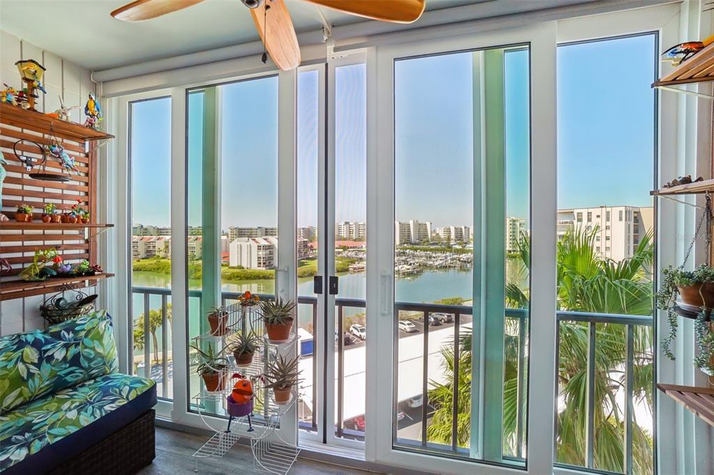 A sunroom features floor-to-ceiling windows overlooking a marina with boats and nearby apartment buildings — 7400 SUN ISLAND DRIVE S UNIT 712, SOUTH PASADENA, FL