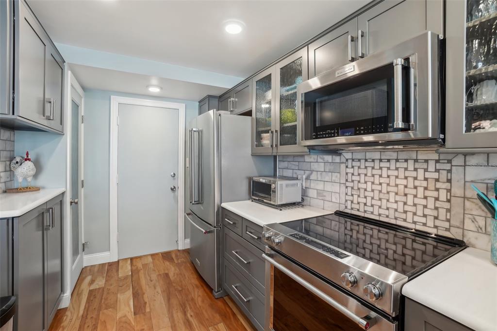 A kitchen features gray cabinets, stainless steel appliances, a tiled backsplash, and wood-look flooring — 7400 SUN ISLAND DRIVE S UNIT 712, SOUTH PASADENA, FL