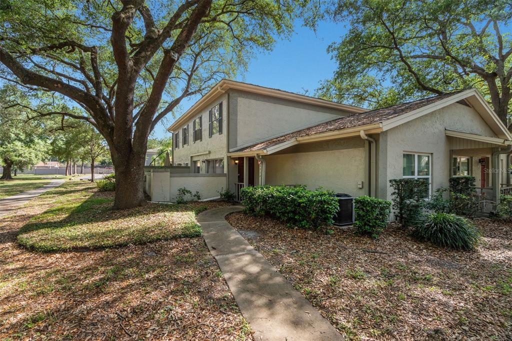 A two-story townhouse exterior with a concrete walkway, mature trees, and a small porch — 6322 TREETOP CIRCLE, TEMPLE TERRACE, FL