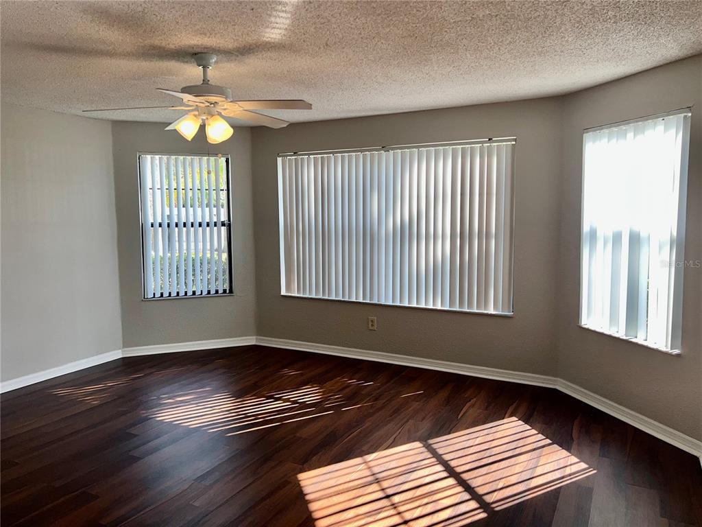 An empty room features dark wood flooring, a ceiling fan, and large windows with blinds — 2807 RIO GRANDE TRAIL UNIT 2807, KISSIMMEE, FL