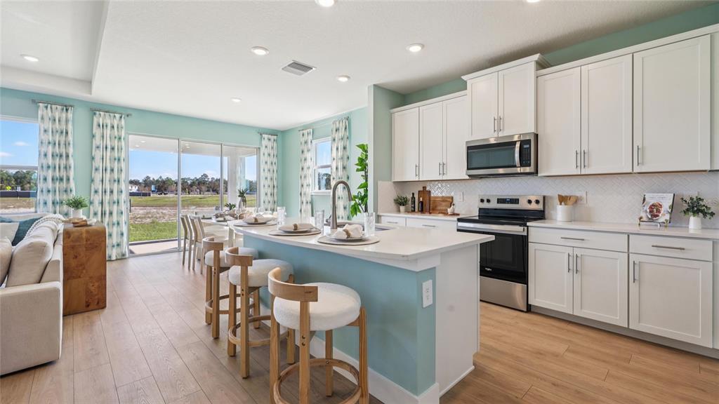 A kitchen with white cabinets, a light blue island, and wood-look flooring opens to a living area — 4201 SW 52ND LANE ROAD, OCALA, FL