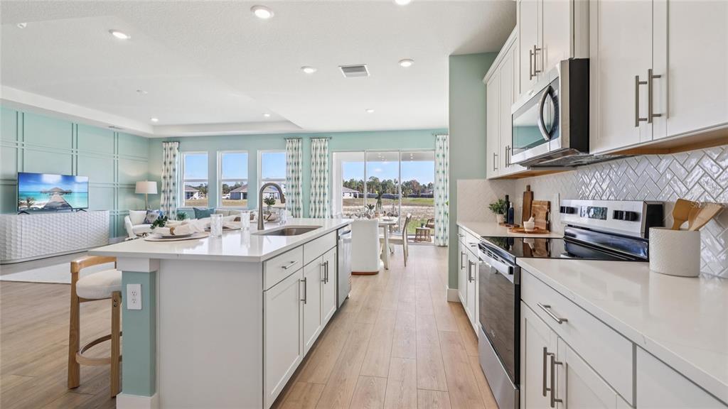 A bright kitchen with white cabinets, quartz countertops, and a large island overlooks the living area — 4201 SW 52ND LANE ROAD, OCALA, FL