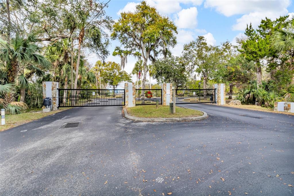 A gated entrance with stone pillars and black metal fencing surrounded by mature trees — 11961 W EDGEVIEW COURT UNIT 11961, CRYSTAL RIVER, FL
