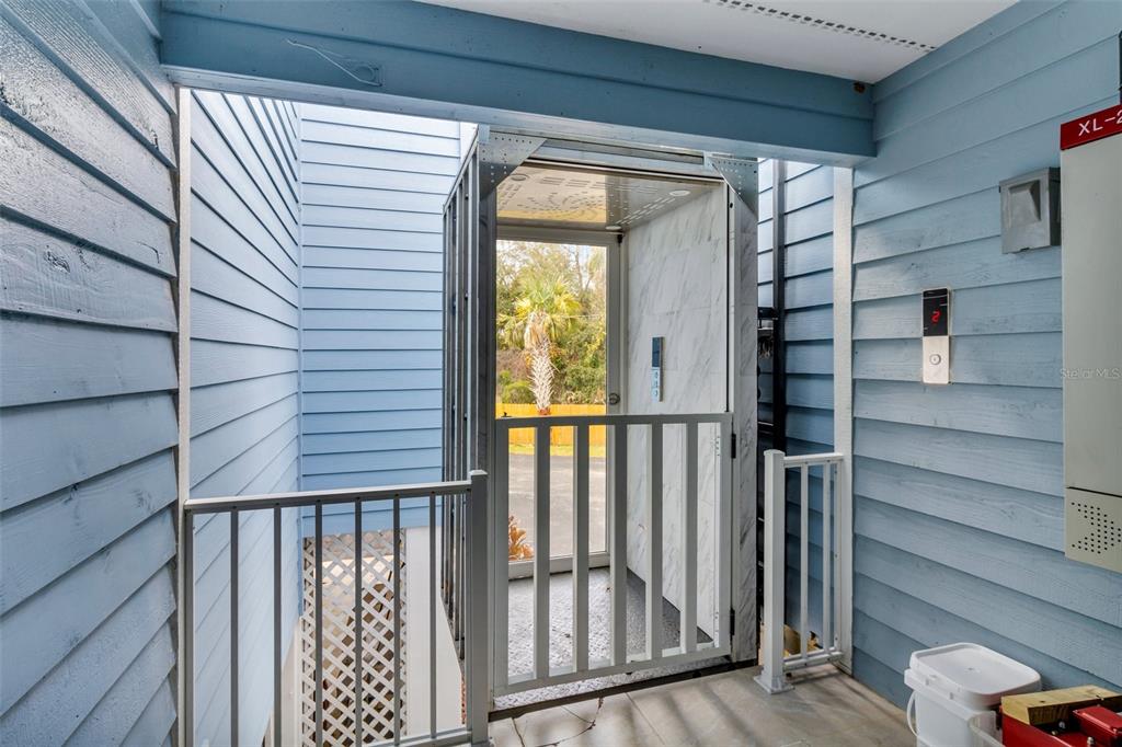 An outdoor residential elevator with a white metal gate sits on a blue-sided porch — 11961 W EDGEVIEW COURT UNIT 11961, CRYSTAL RIVER, FL