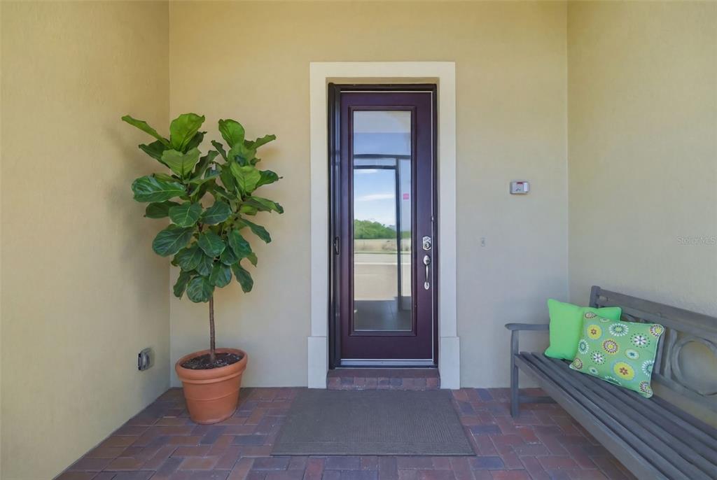 A covered entryway features a dark-framed glass door, a potted plant, and a wooden bench — 10730 IRONBRIDGE DRIVE, VENICE, FL