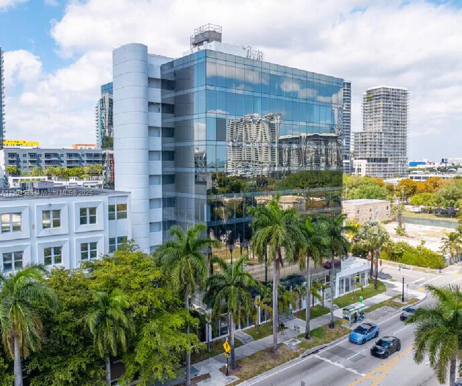 A modern glass-facade office building stands next to a white structure with palm trees — 3050 Biscayne Blvd # 702, Miami FL 33137, MIAMI, FL
