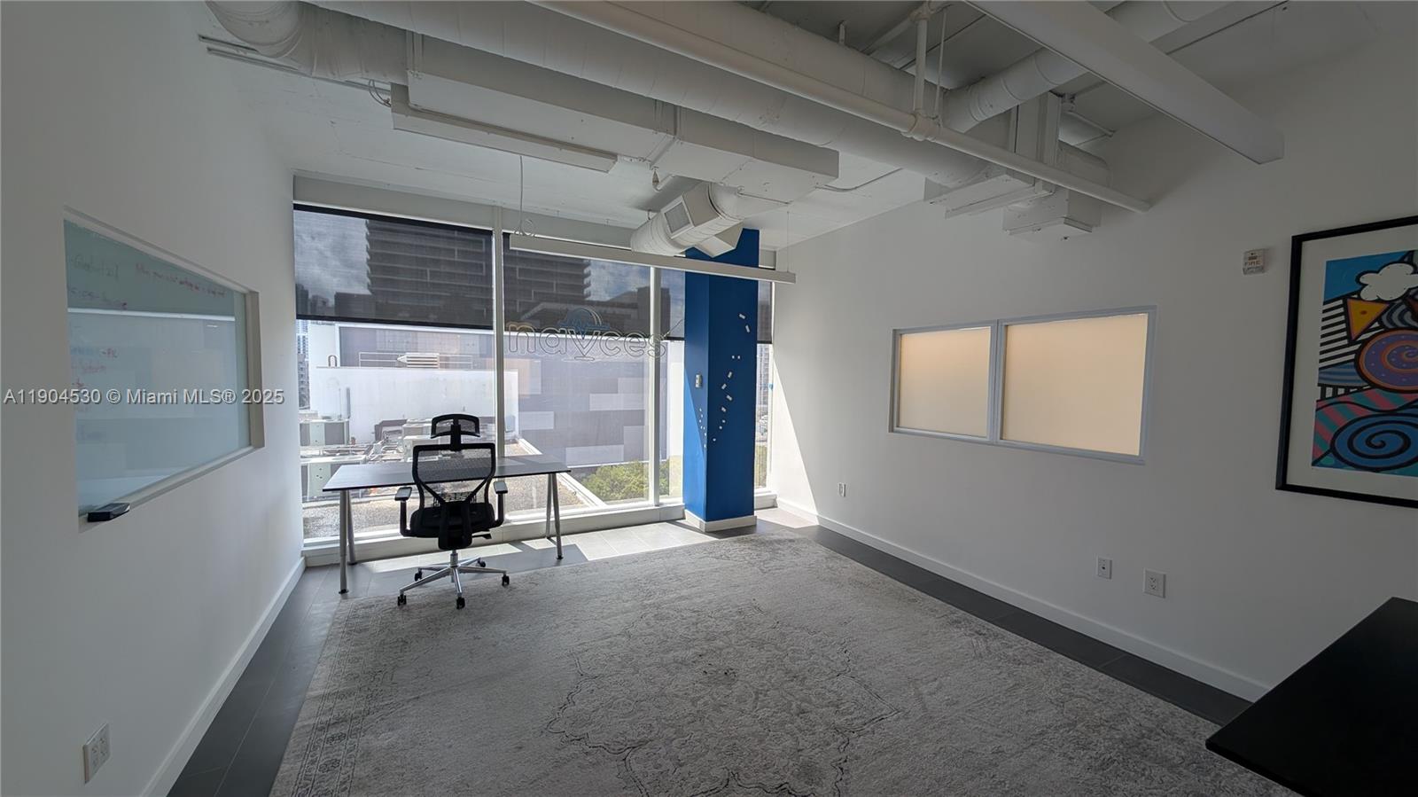 An office space features a desk, chair, large rug, whiteboard, and a blue support column — 3050 Biscayne Blvd # 702, Miami FL 33137, MIAMI, FL