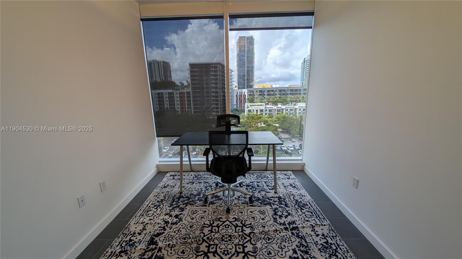 A home office features a desk, an ergonomic chair, a patterned rug, and floor-to-ceiling windows — 3050 Biscayne Blvd # 702, Miami FL 33137, MIAMI, FL