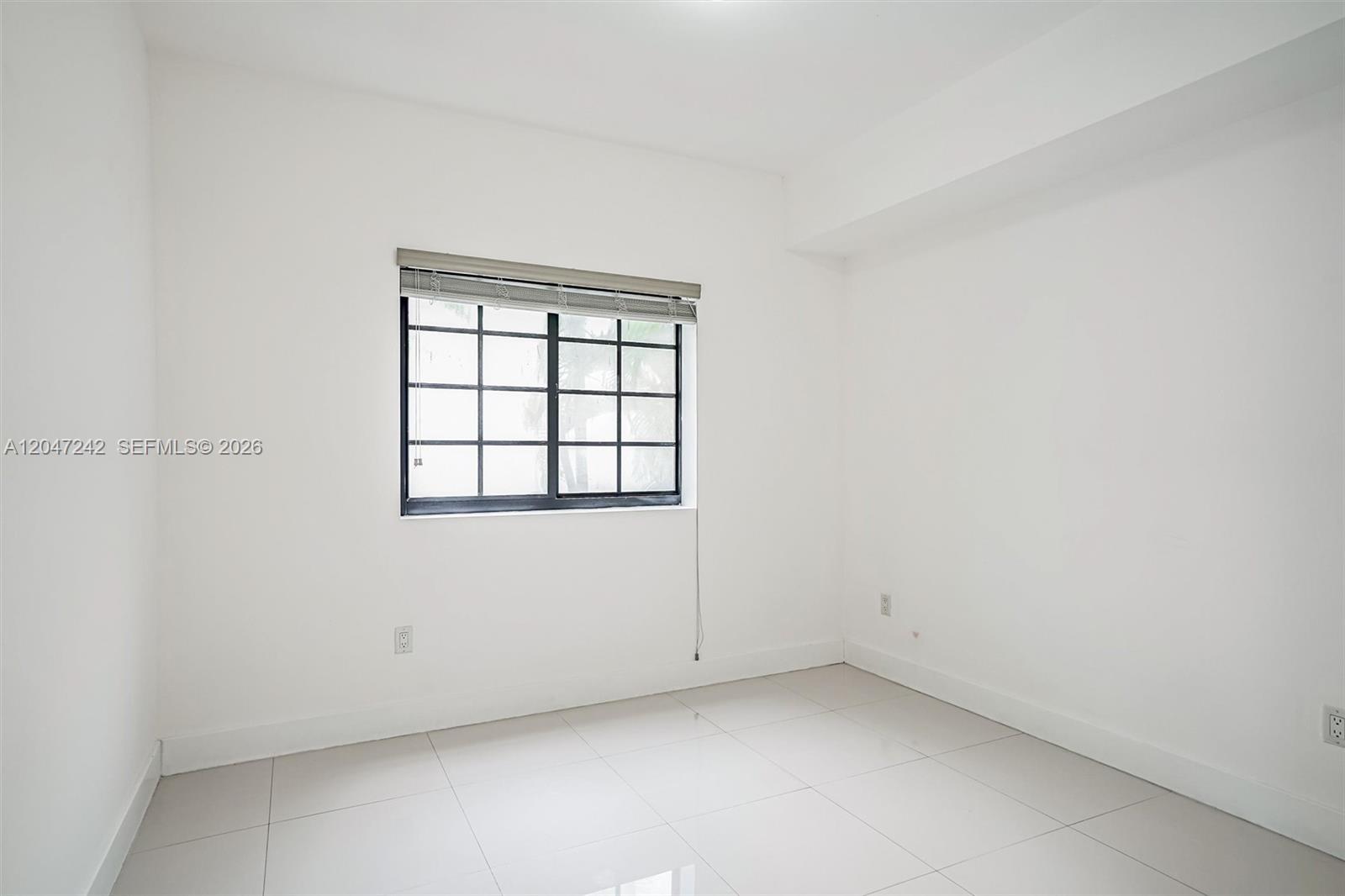 An empty room features white walls, light-colored tile flooring, and a window with black grids — 1901 S Le Jeune Rd # 2, Coral Gables FL 33134, CORAL GABLES, FL