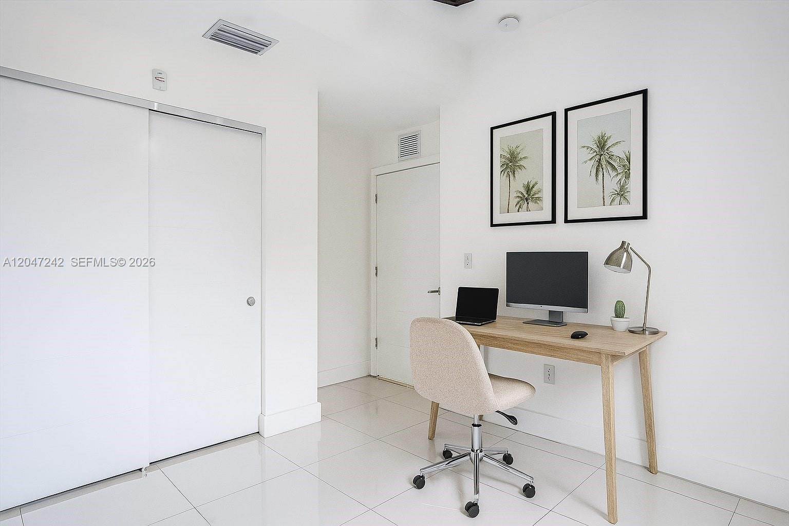 A home office features a wooden desk, a rolling chair, and wall art on white walls — 1901 S Le Jeune Rd # 2, Coral Gables FL 33134, CORAL GABLES, FL