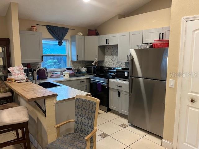 A kitchen features gray cabinets, stainless steel appliances, a butcher block breakfast bar, and tile flooring — 4001 KALUGA PARK STREET, ORLANDO, FL
