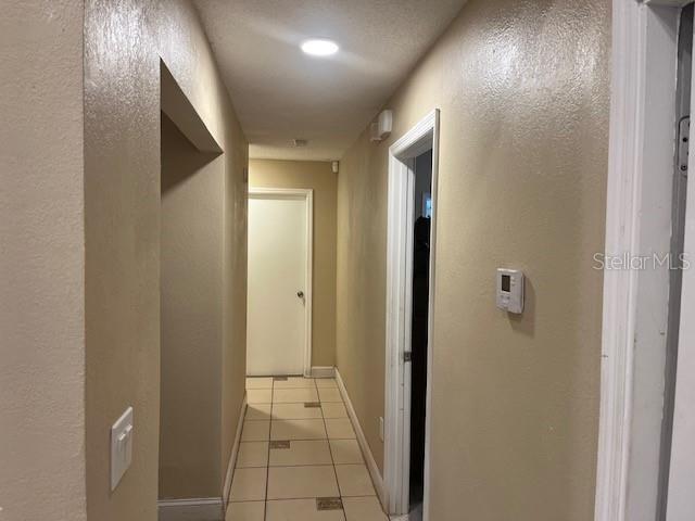 A hallway with beige walls, tiled flooring, and multiple doorways leading to other rooms — 4001 KALUGA PARK STREET, ORLANDO, FL