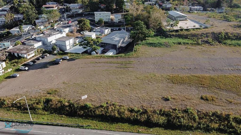 An aerial view shows a large, vacant dirt lot adjacent to a paved road and buildings — 0 CARR DM #2-166.6, HORMIGUEROS, PR