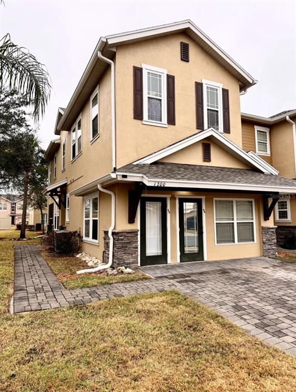 A two-story tan stucco townhouse features a stone-accented base, dark shutters, and a paved walkway — 1200 TETON DRIVE, KISSIMMEE, FL