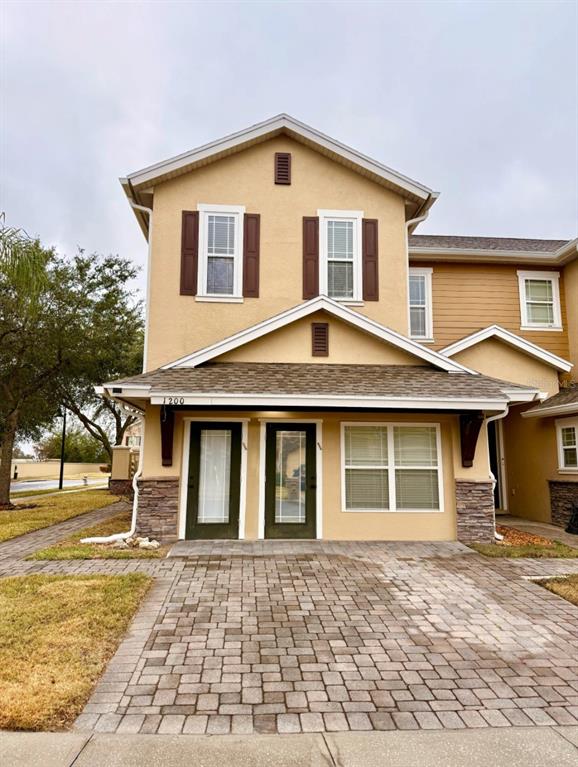 A two-story townhouse exterior features tan stucco, brown shutters, a stone base, and a paver driveway — 1200 TETON DRIVE, KISSIMMEE, FL